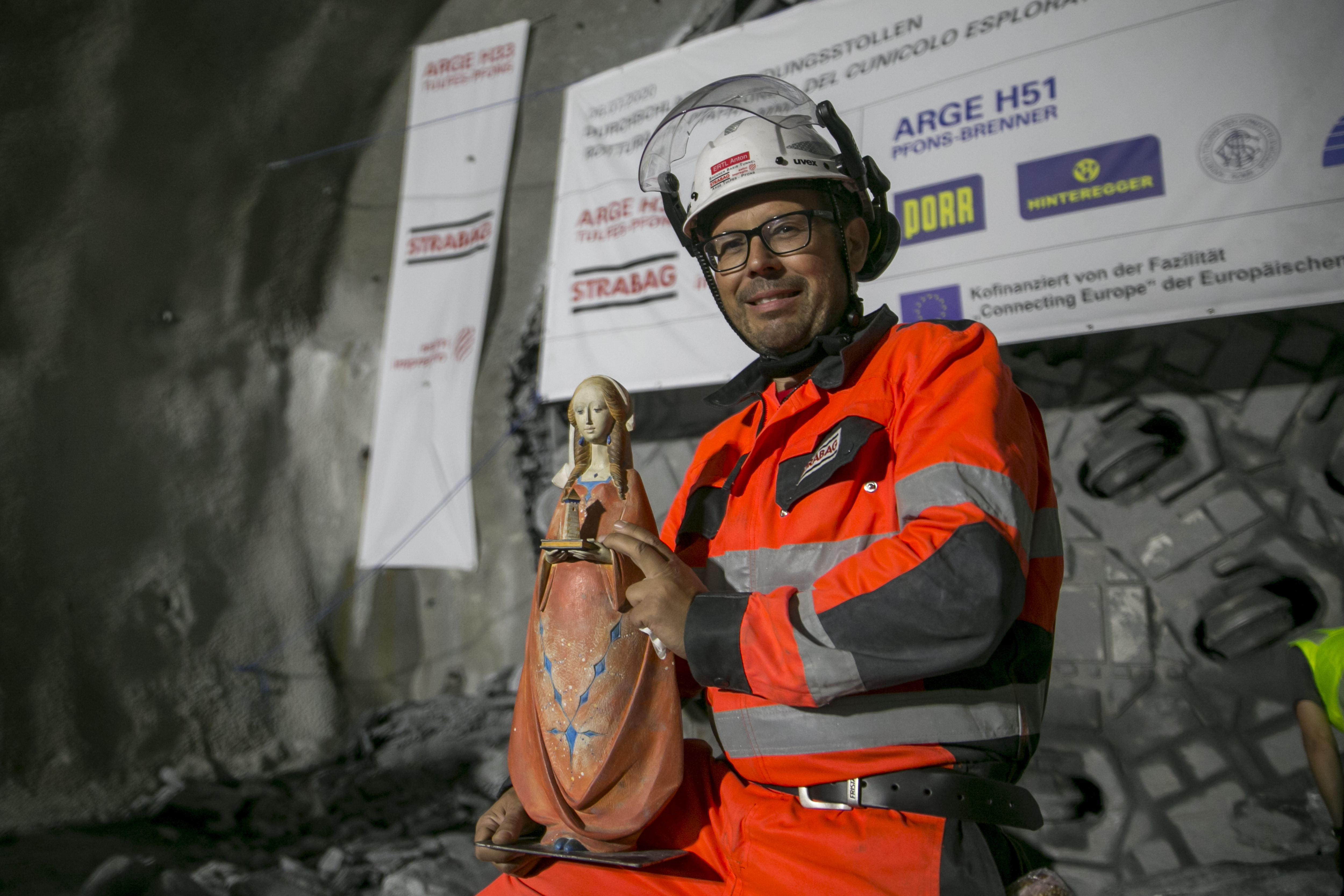 Foto eines Tunnelbauarbeiters in Schutzkleidung, er hält eine Madonna Figur in den Händen