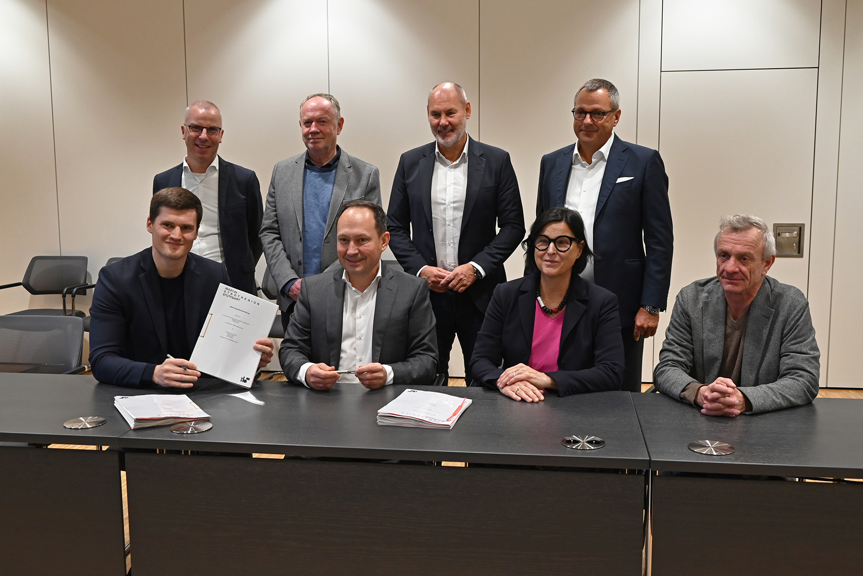 Foto von mehreren freundlich schauenden Personen die an einem Tisch sitzen. 
